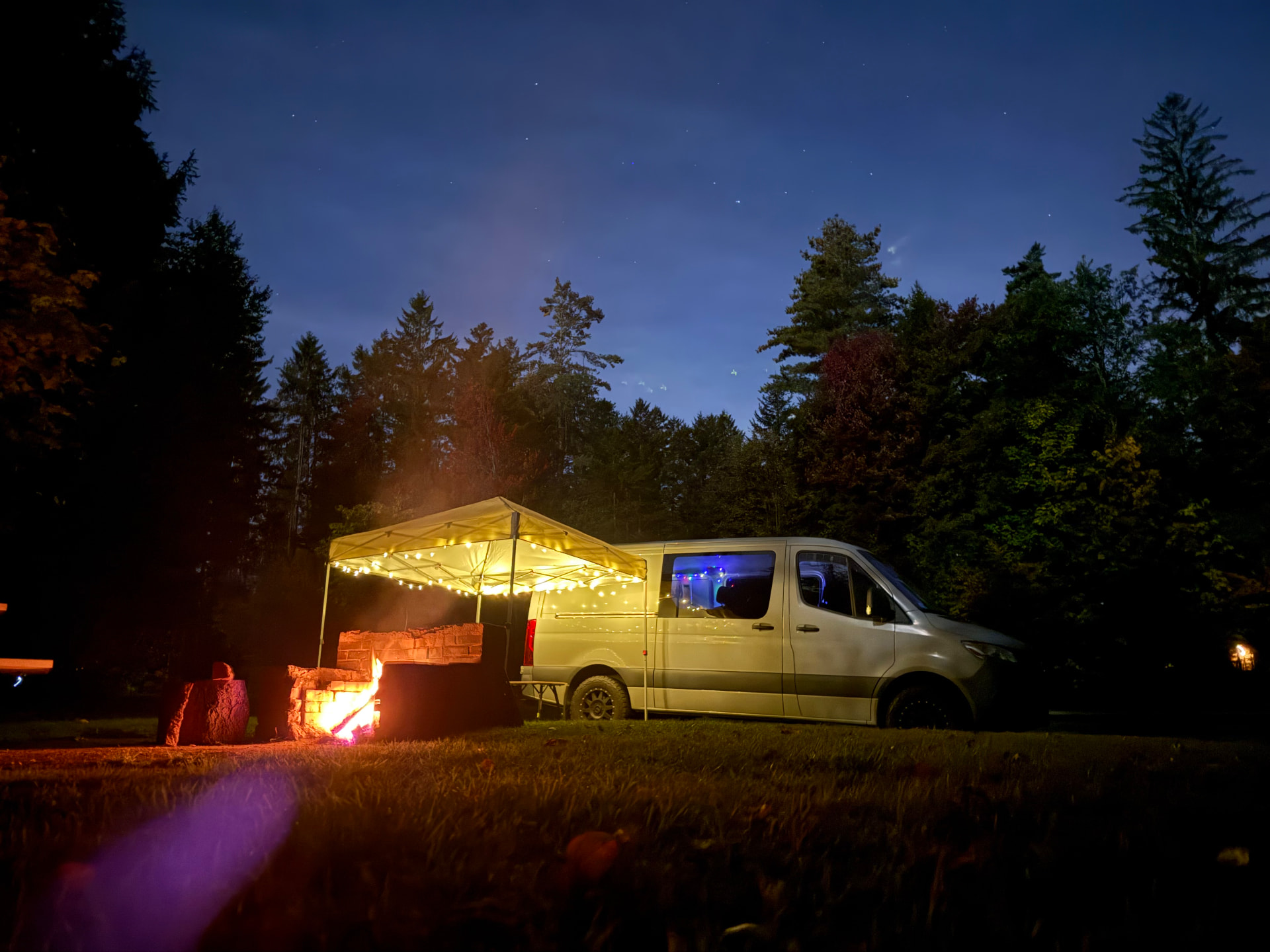 Sprinter campsite under the stars with a glowing canopy and campfire