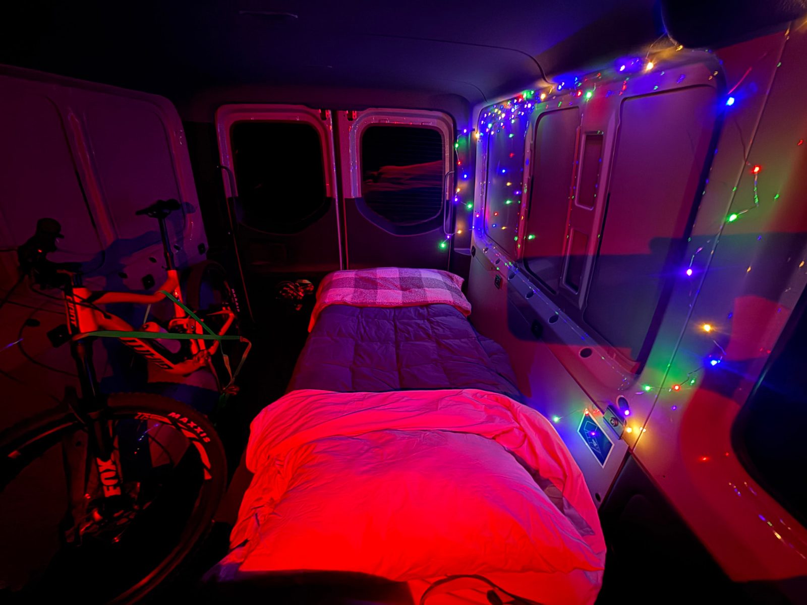 Van bed at night with string lights and the mountain bike strapped alongside